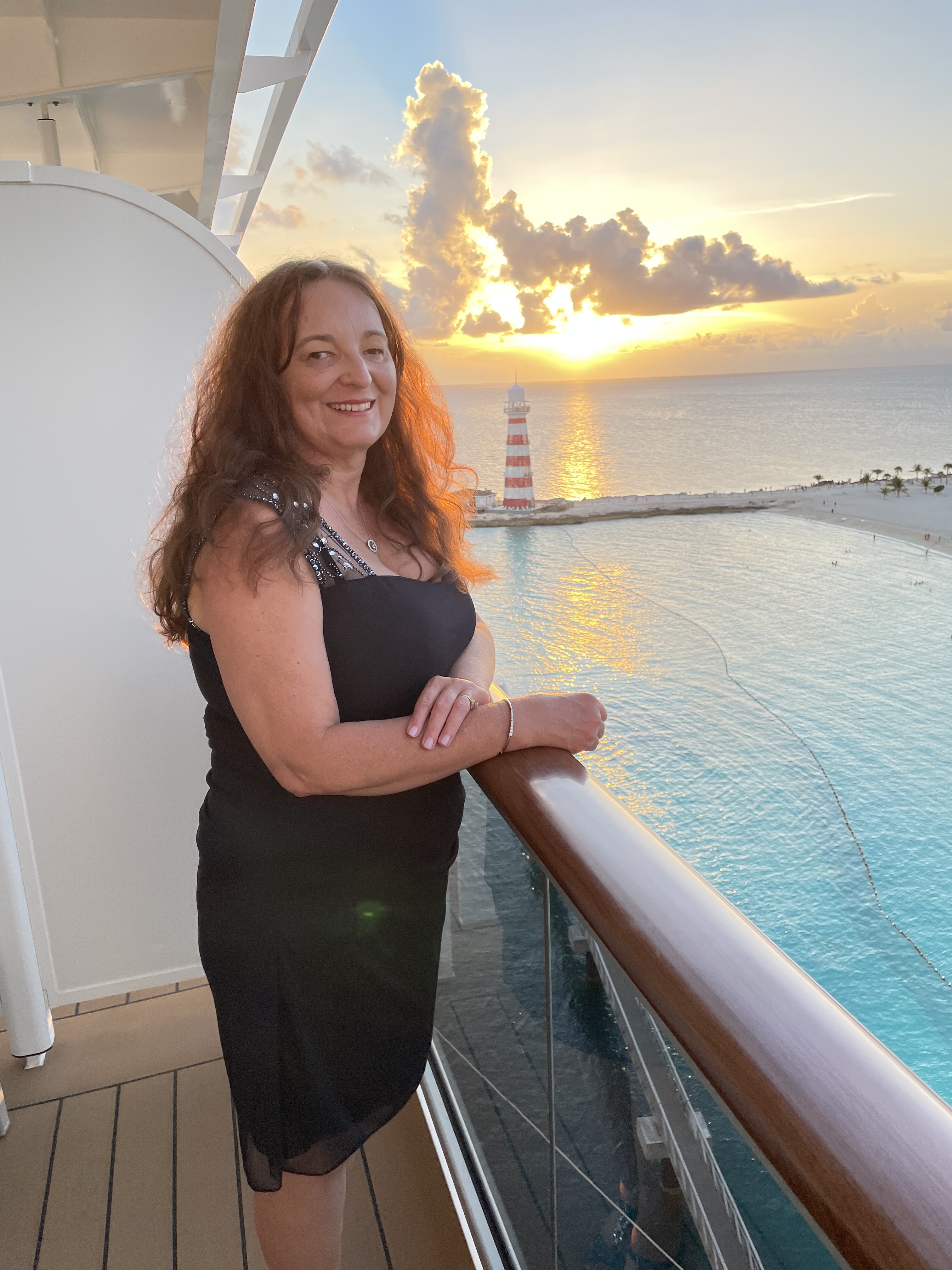 Sylvia is standing on the deck of a boat, she has long dark hair and is wearing a purple dress.